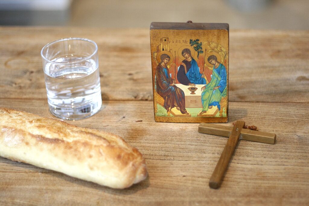 Pão e aguá ao lado de uma pequena cruz de madeira e um pequeno ícone de rublev que representa a trindade santa.